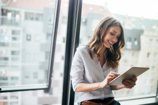 Attractive businesswoman using a digital tablet while standing in front of windows Attractive businesswoman using a digital tablet while standing in front of windows