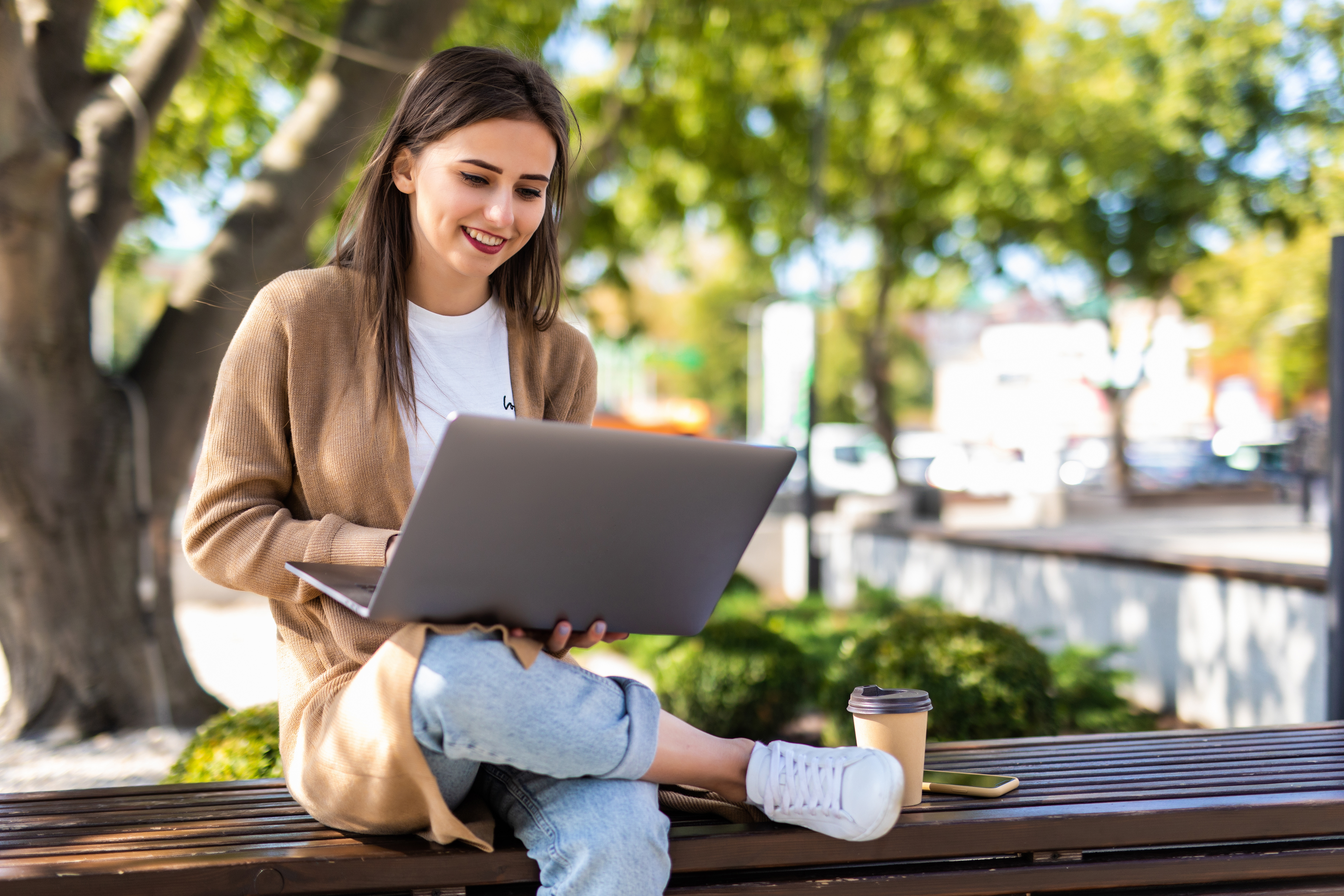 Young beautiful business woman working on a laptop sitting on the bench in the street sitzende Frau vor einem Laptop.