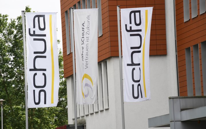Zwei Fahnen des Schufa-Logos hängend an einer Gebäudefront.