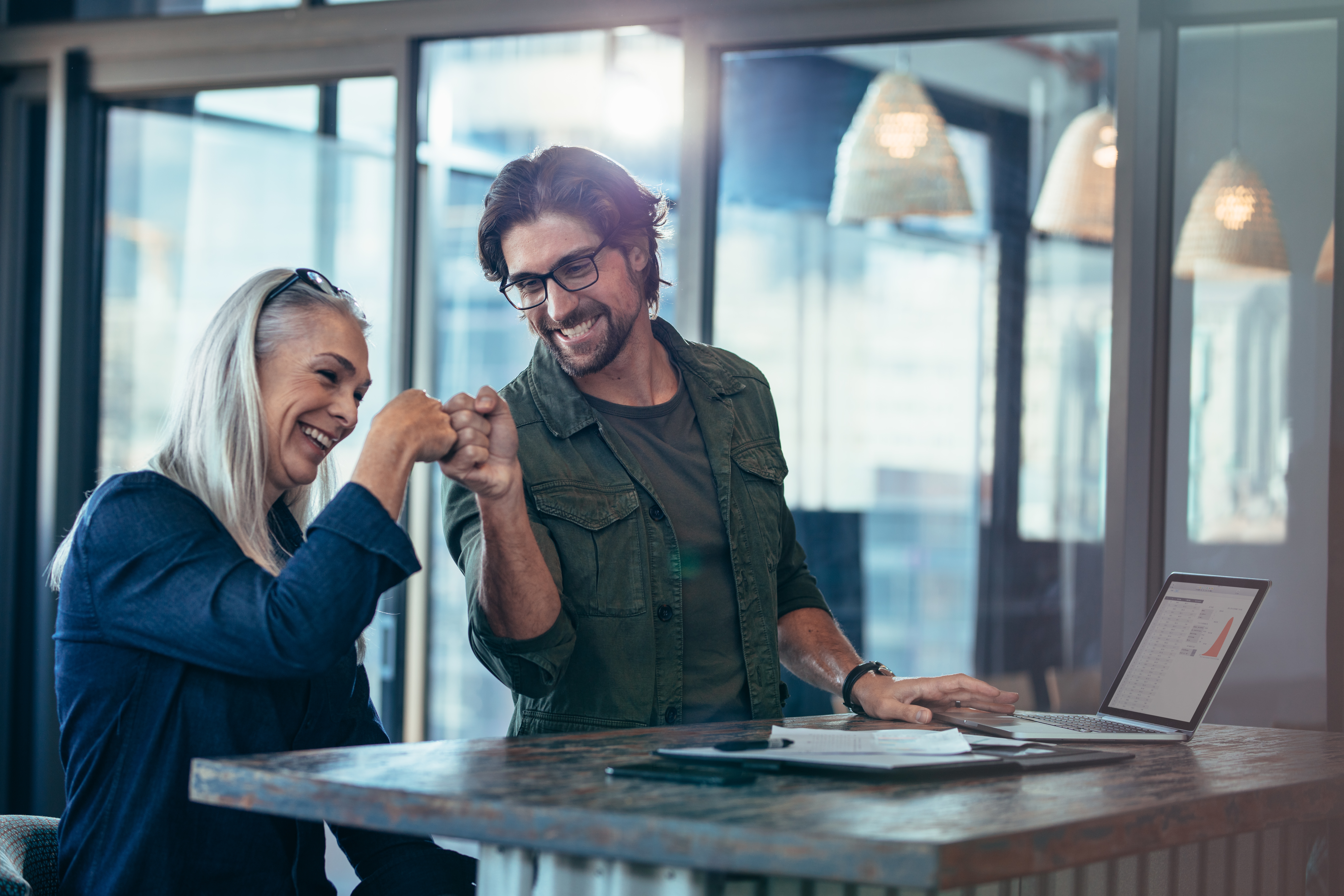 Business colleagues making a fist bump at office Eine Frau und ein Mann machen einen Fauststoss in einer Büroumgebung.