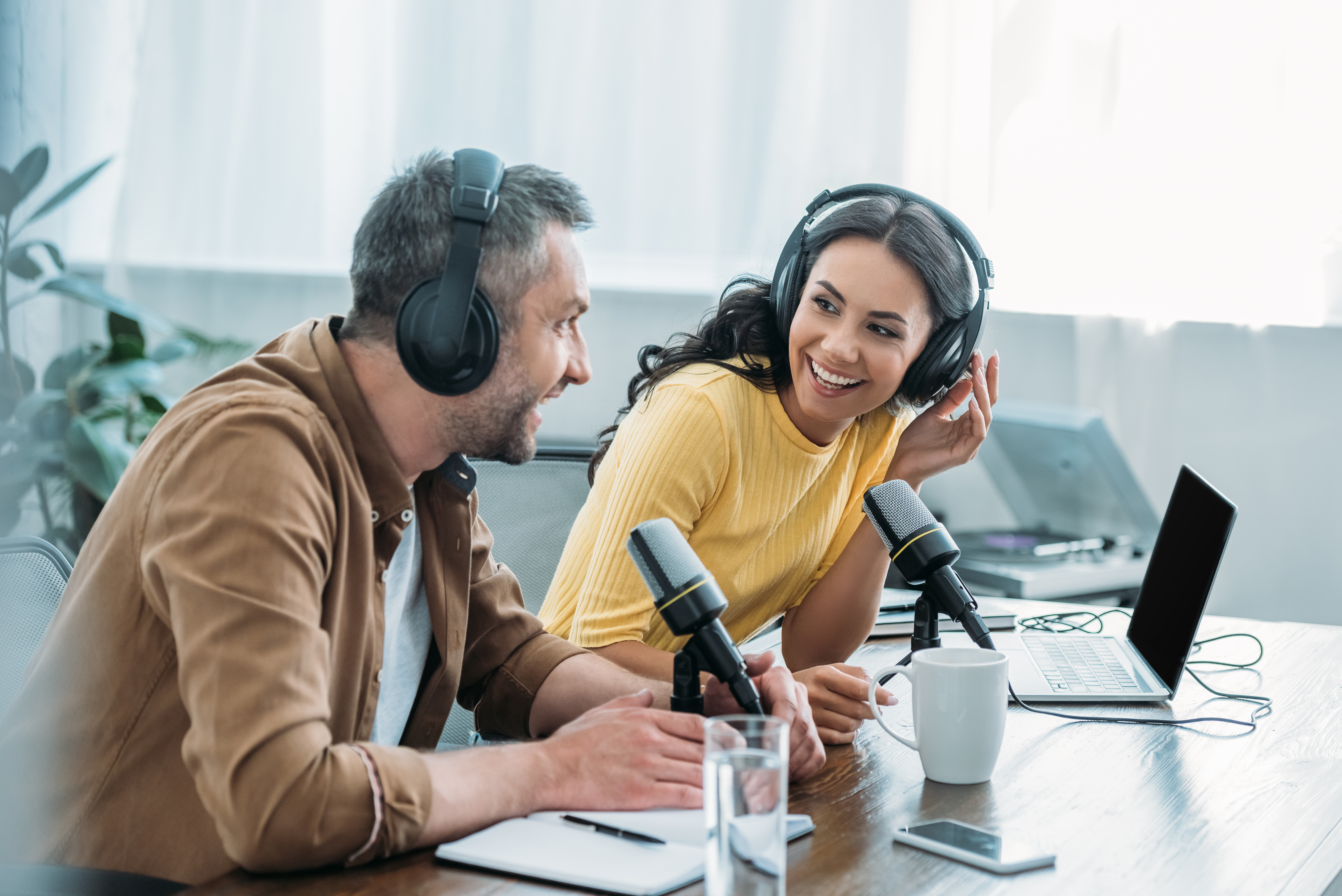 Zwei Personen mit Headset und Mikrofon vor einem Schreibtisch.