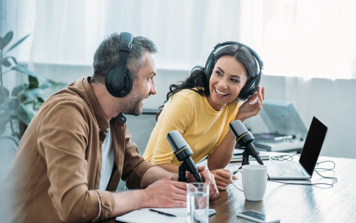 Zwei Personen mit Headset und Mikrofon vor einem Schreibtisch.
