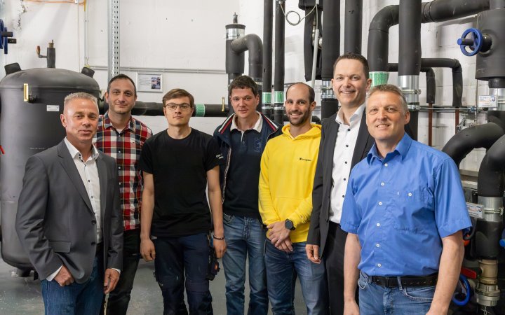 Björn Brede und weitere Personen vor einer Wärmepumpen-Anlage.