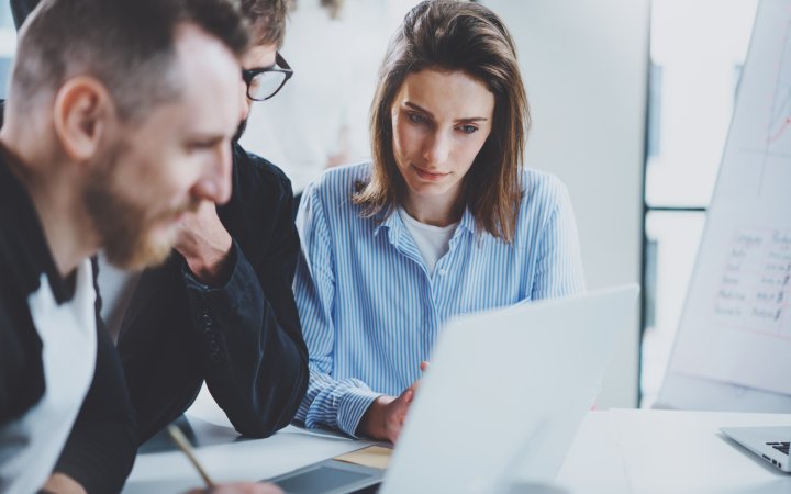 Three coworkers at working process.Young woman working together with colleague at modern office.Teamwork concept. Blurred background.Horizontal.