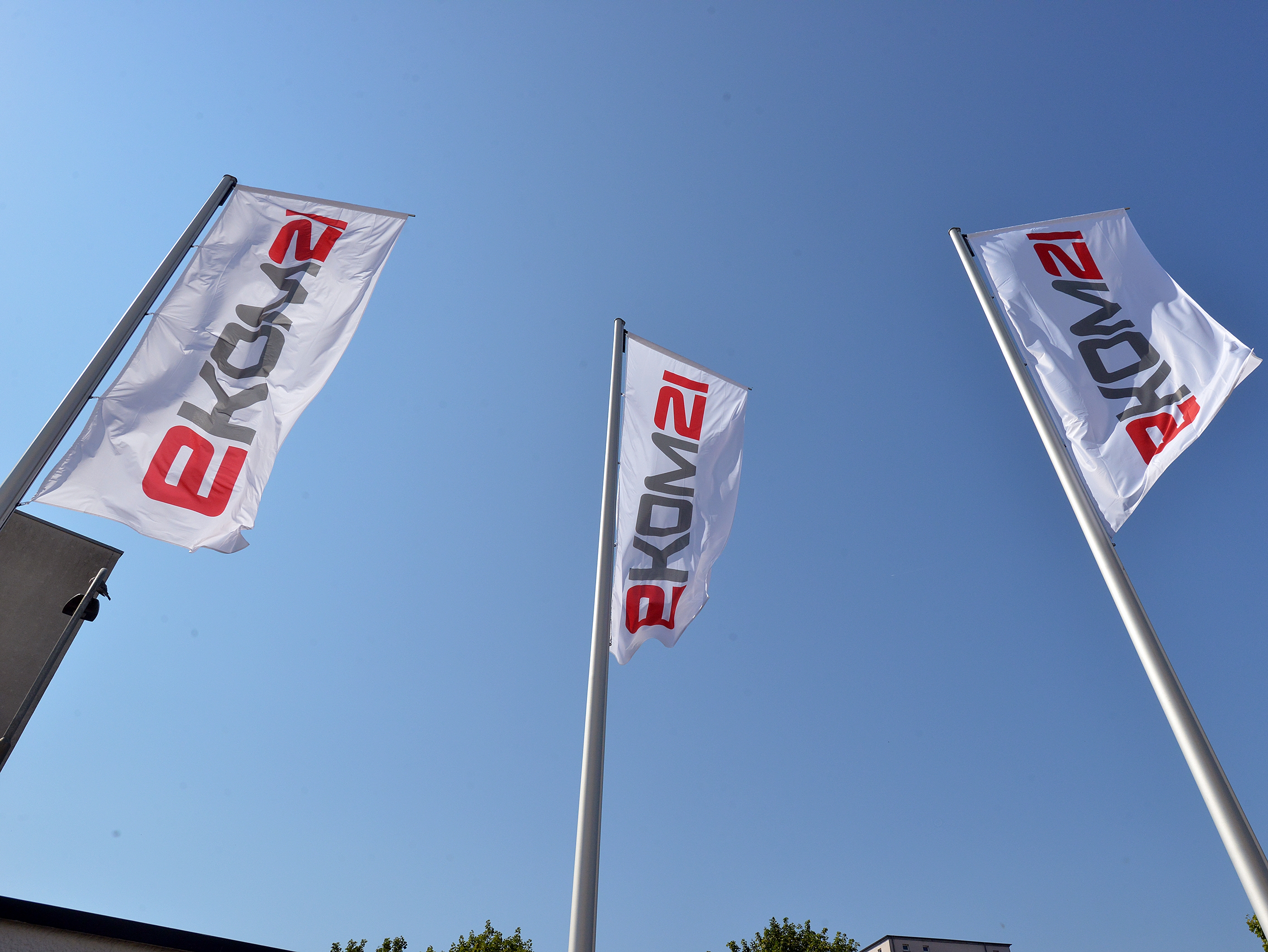 Drei Fahnenmäste mit Fahnen; auf den Fahnen Logo der ekom21