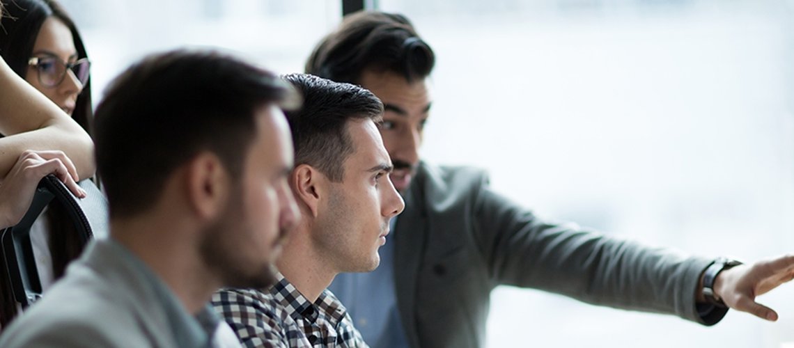 Fünf Personen vor einem Computer; ein Mann zeigt auf den Computer