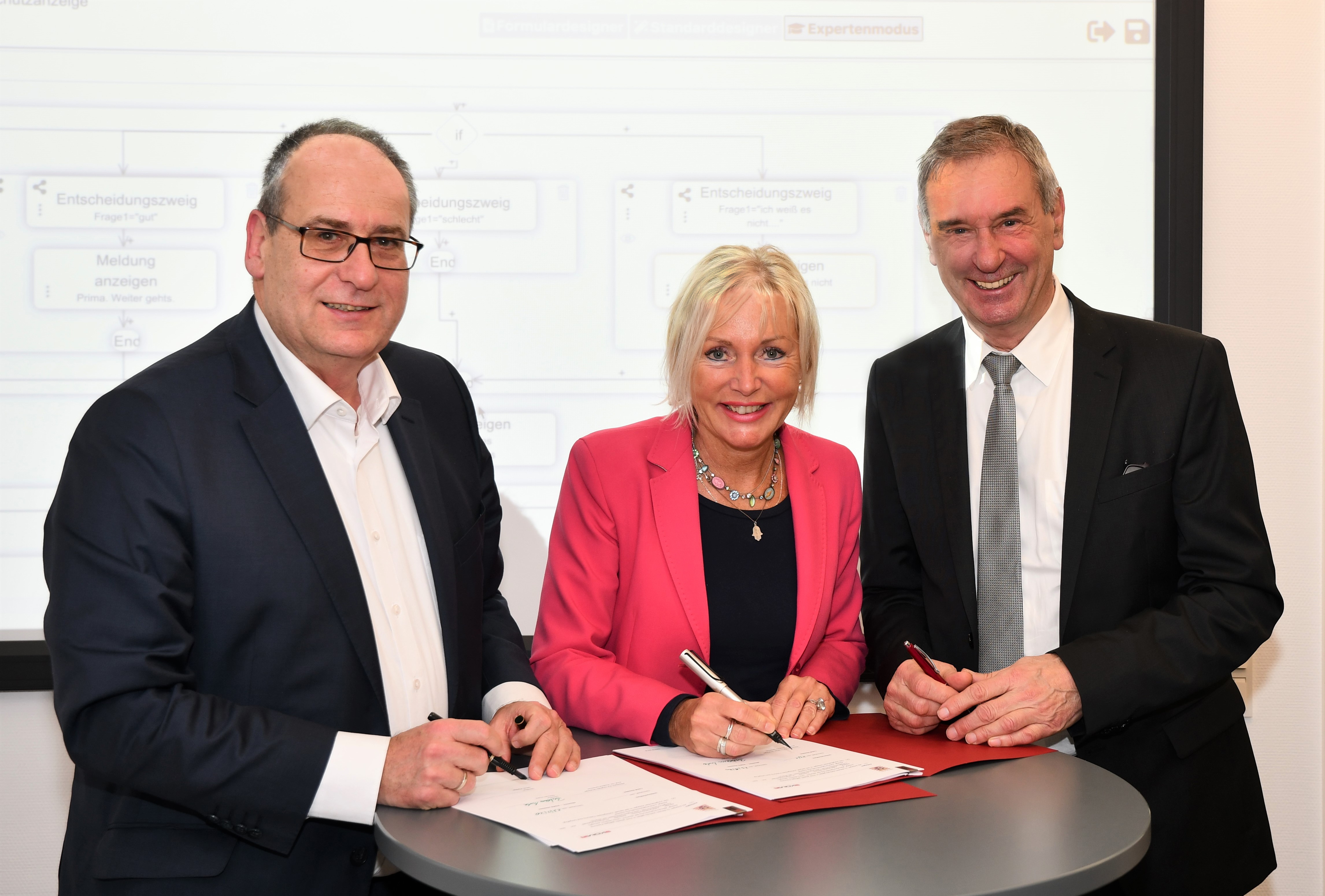Kristina Sinemus bei der Unterzeichnung eines Dokuments und zwei weitere Personen.