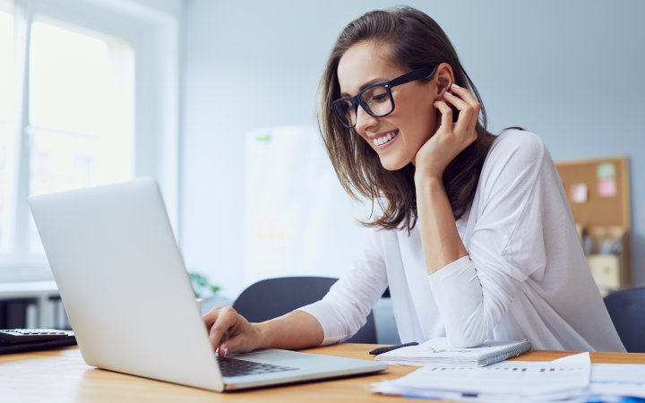 Sitzende Frau arbeitet mit einem Laptop; welcher vor ihr auf einem Tisch steht.