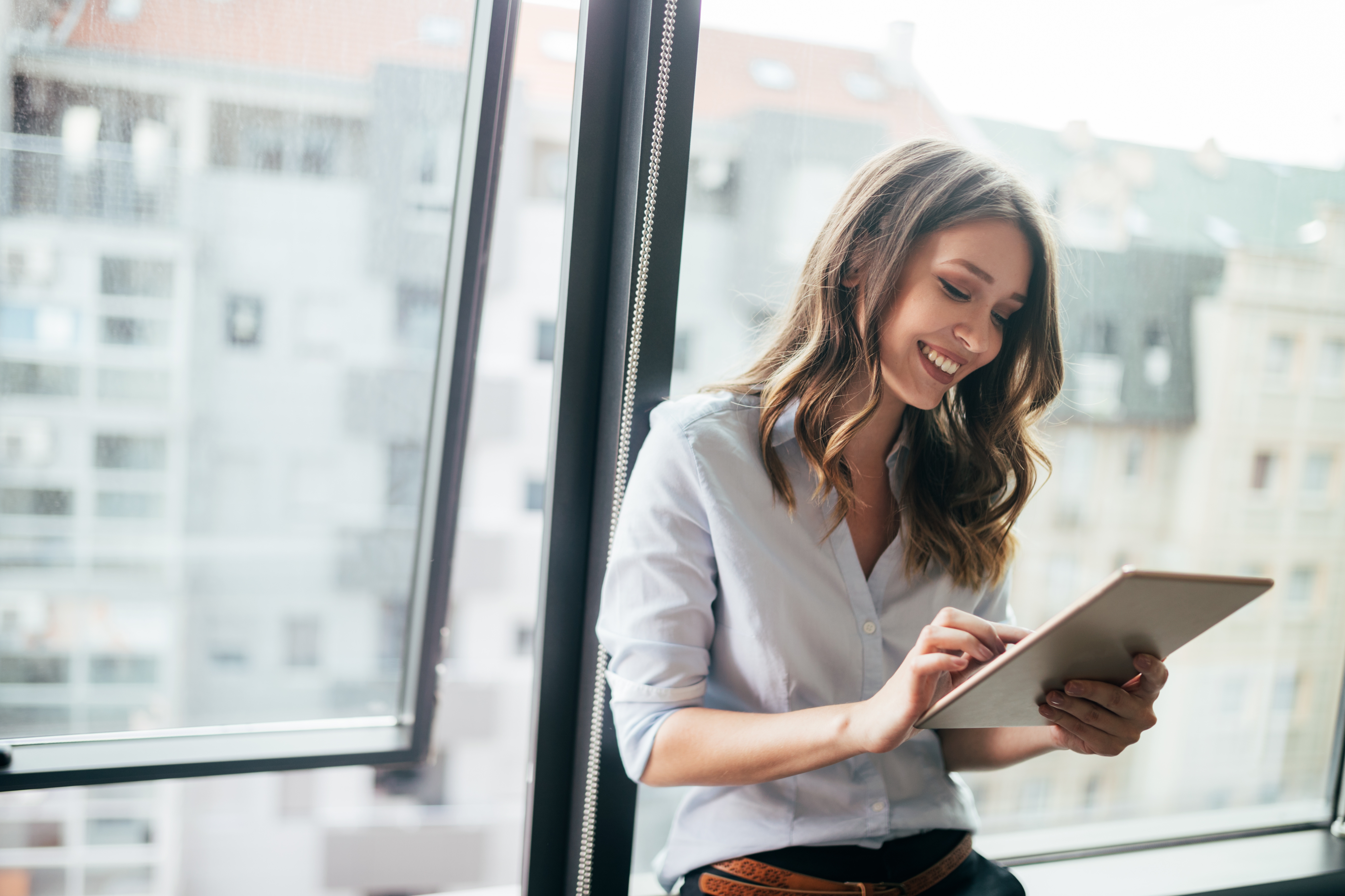 Attractive businesswoman using a digital tablet while standing in front of windows Attractive businesswoman using a digital tablet while standing in front of windows