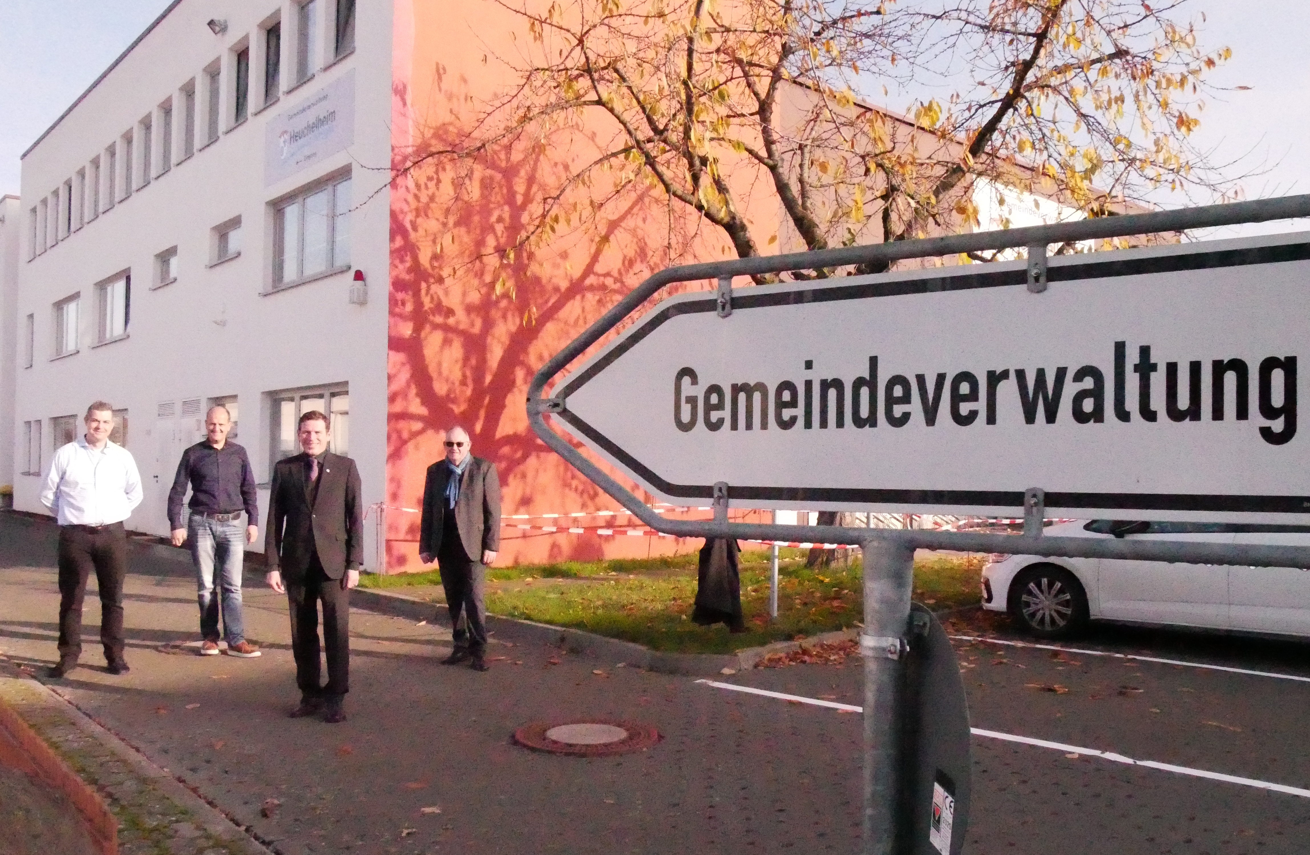 Gruppe von Personen; im Vordergrund ein Schild mit der Aufschrift Gemeindeverwaltung.