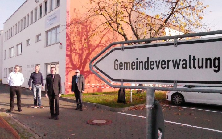 Gruppe von Personen; im Vordergrund ein Schild mit der Aufschrift Gemeindeverwaltung.