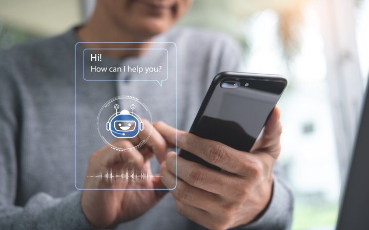 Ausschnitt eines Programms; im Hintergrund hält ein Mann ein Smartphone.