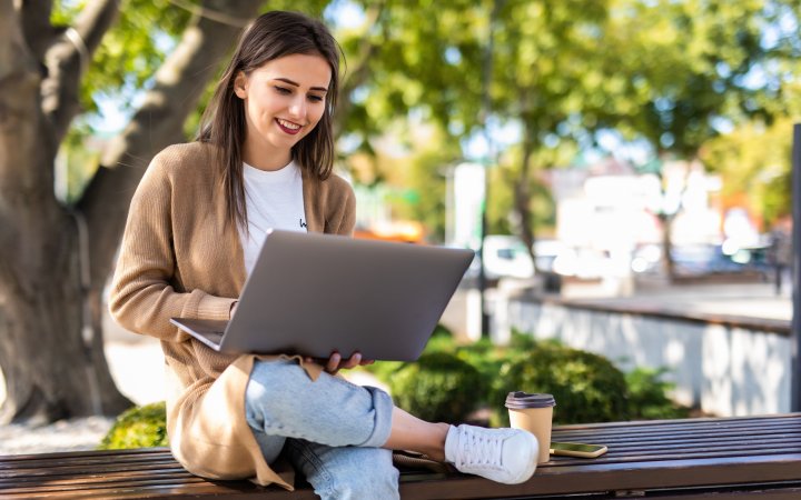 Young beautiful business woman working on a laptop sitting on the bench in the street