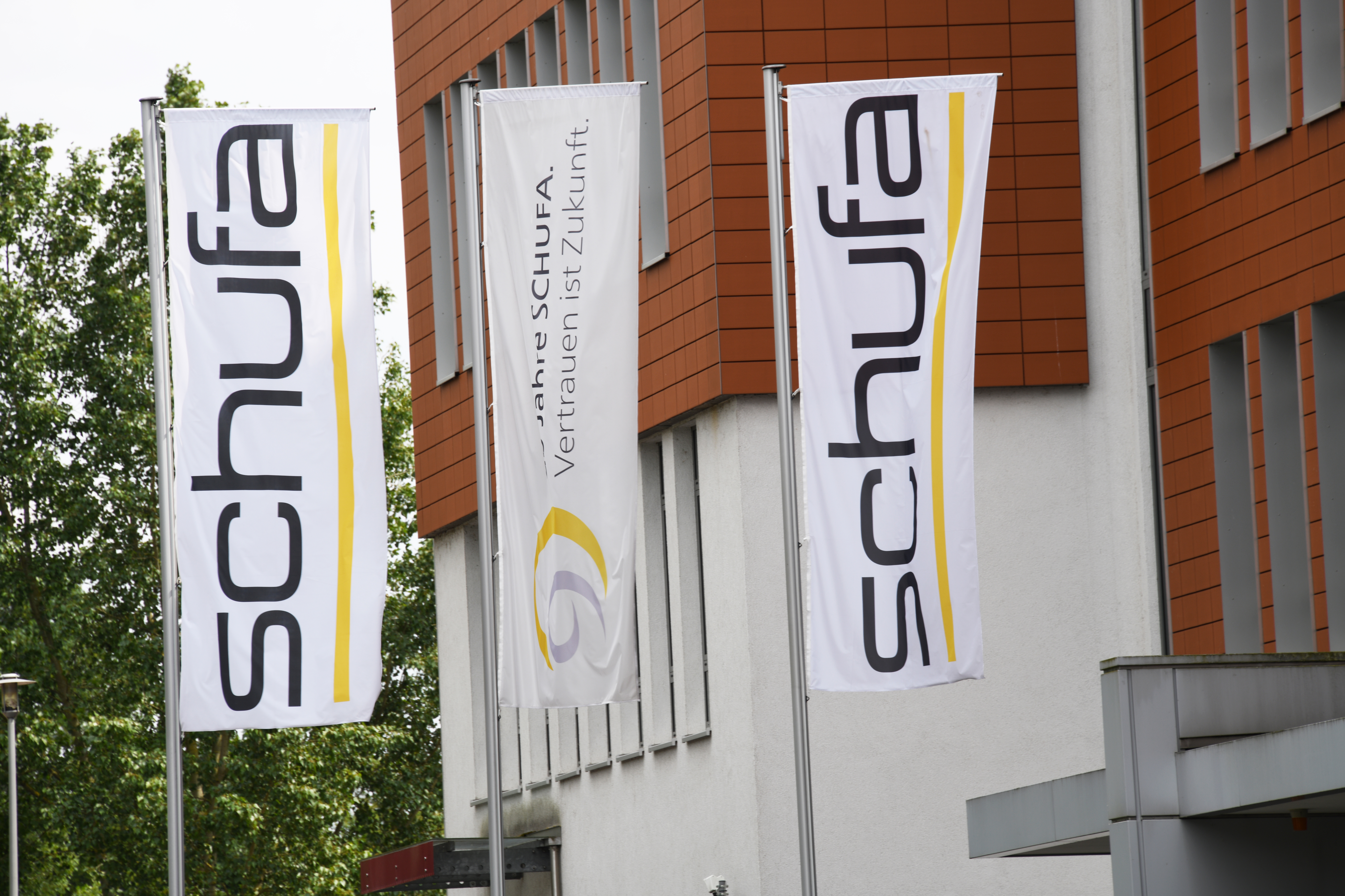 Zwei Fahnen des Schufa-Logos hängend an einer Gebäudefront.