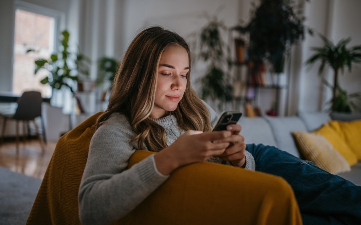 Frau sitzend; blickt in ihr Handy.