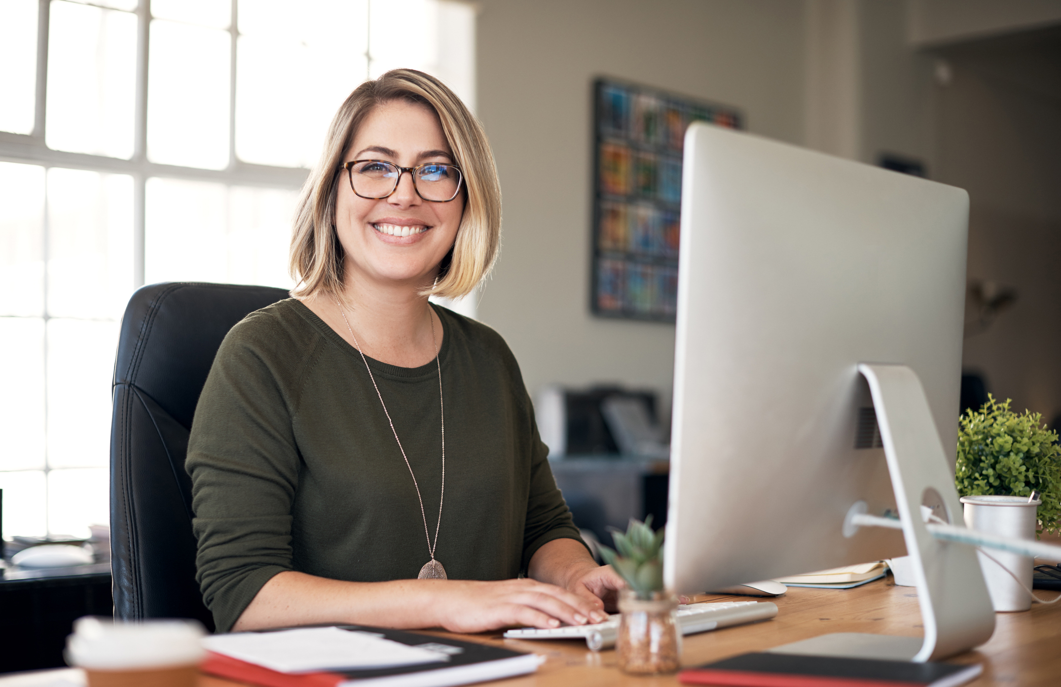 Eine sitzende Frau am Arbeitsplatz in einer Büroumgebung.