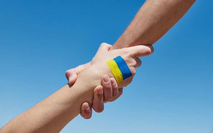 Zwer Personen; die sich die Hände reichen mit aufgetragener Ukraine-Flagge.