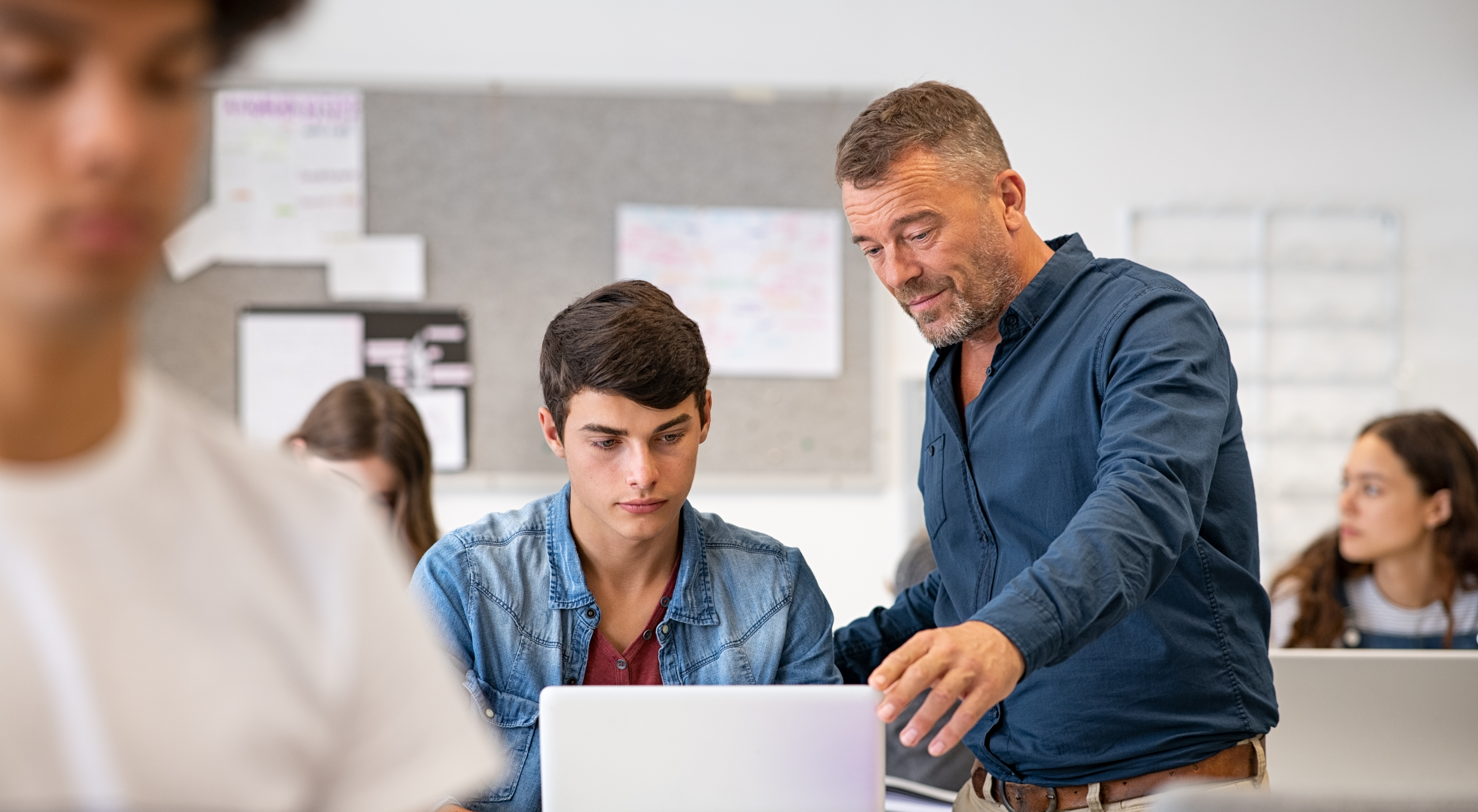 Lehrer im Unterrichtskontext; welcher einem Schüler etwas am Computer zeigt.