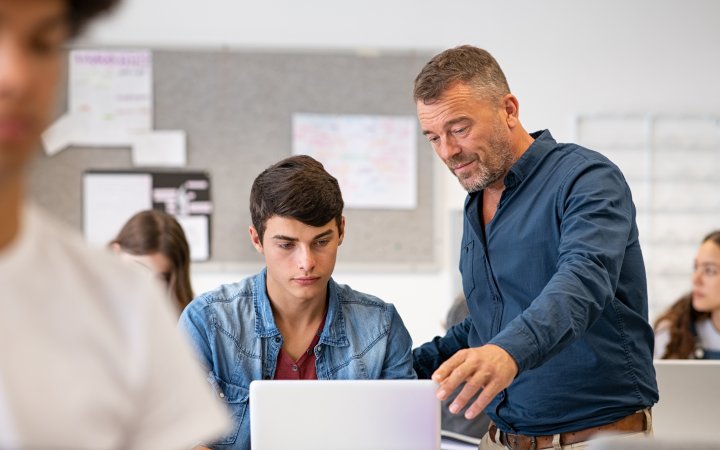 Lehrer im Unterrichtskontext; welcher einem Schüler etwas am Computer zeigt.