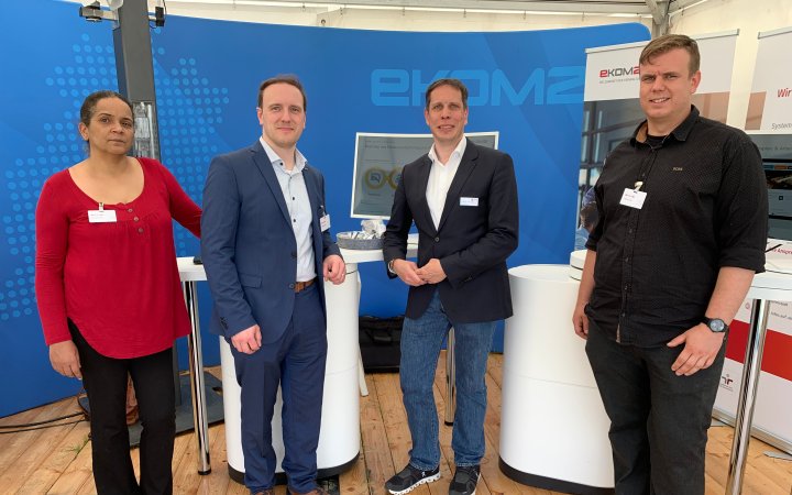 Vier Mitarbeitende vor einem Stand der ekom21.