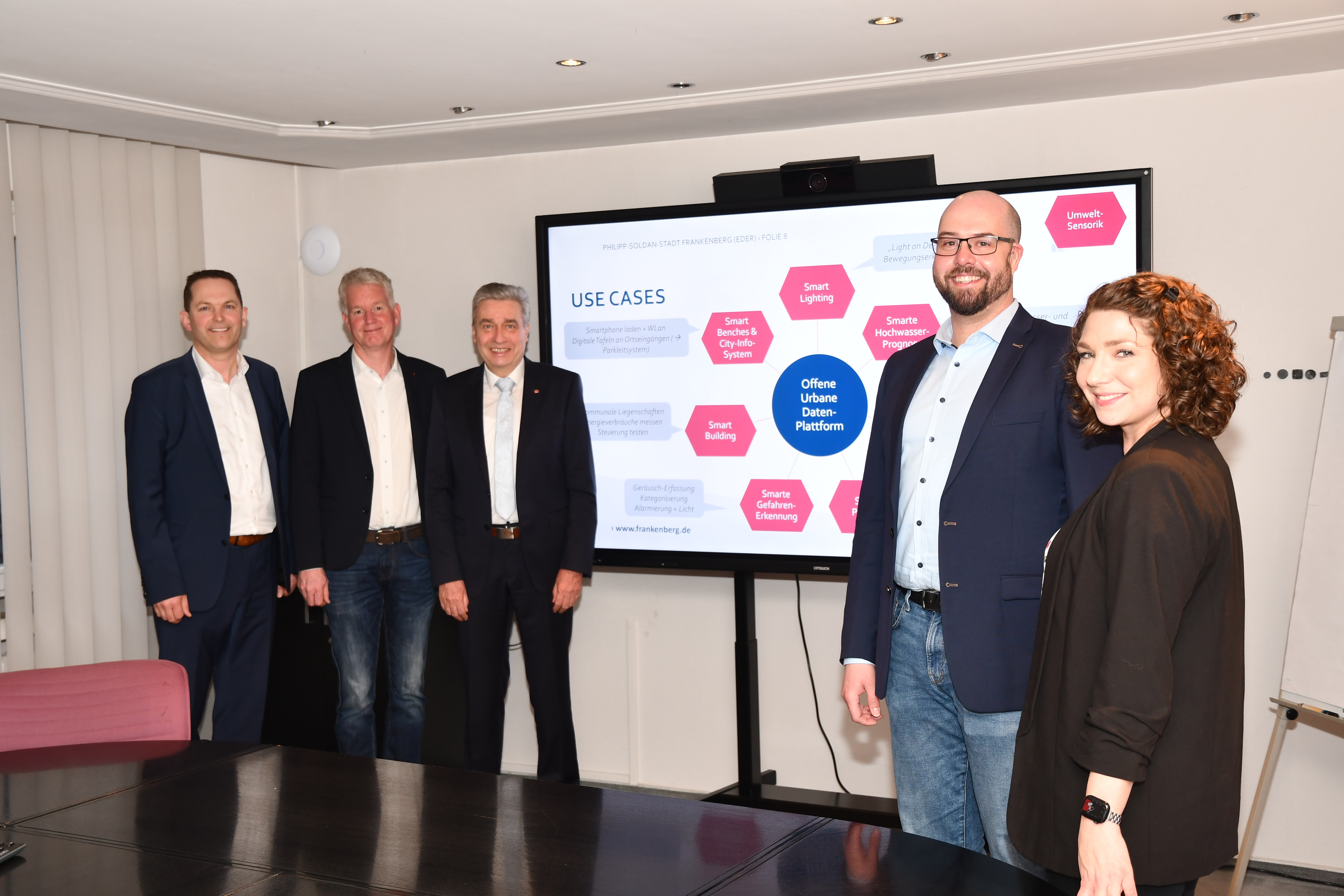 Thea Januschewski; Björn Brede und drei weitere Personen der Gemeinde Frankenberg vor einer Übersichtsdarstellung  von Smart City.