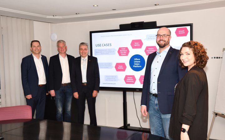 Thea Januschewski; Björn Brede und drei weitere Personen der Gemeinde Frankenberg vor einer Übersichtsdarstellung  von Smart City.