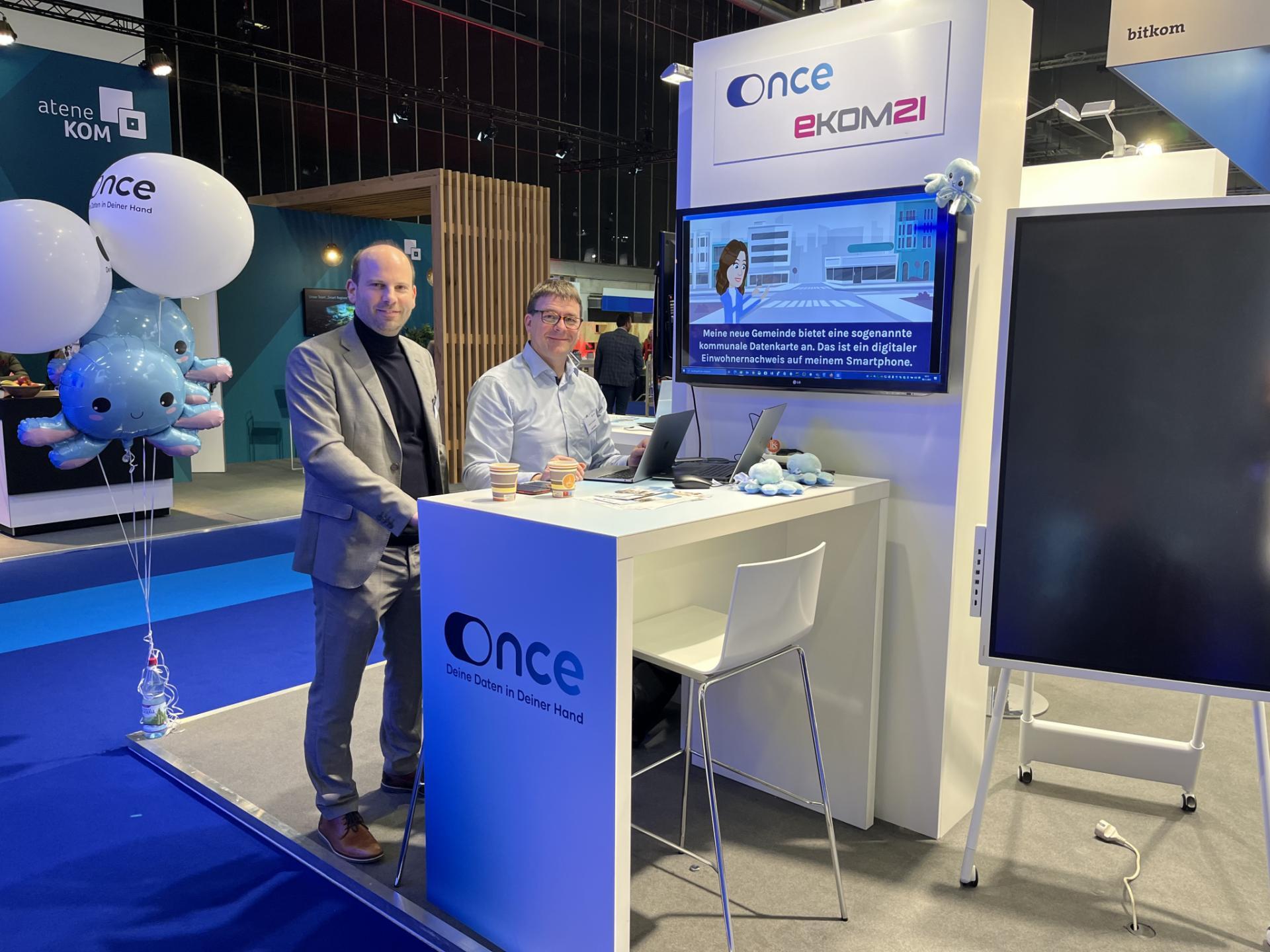 Zwei Personen an einem Stand der ekom21 während einer messeartigen Veranstaltung. 