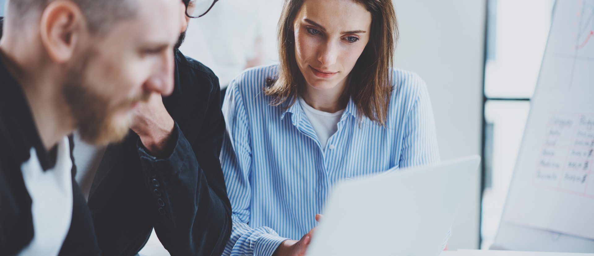 Three coworkers at working process.Young woman working together with colleague at modern office.Teamwork concept. Blurred background.Horizontal.