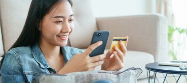 Eine junge Frau hält ein Handy und eine Geldkarte vor sich