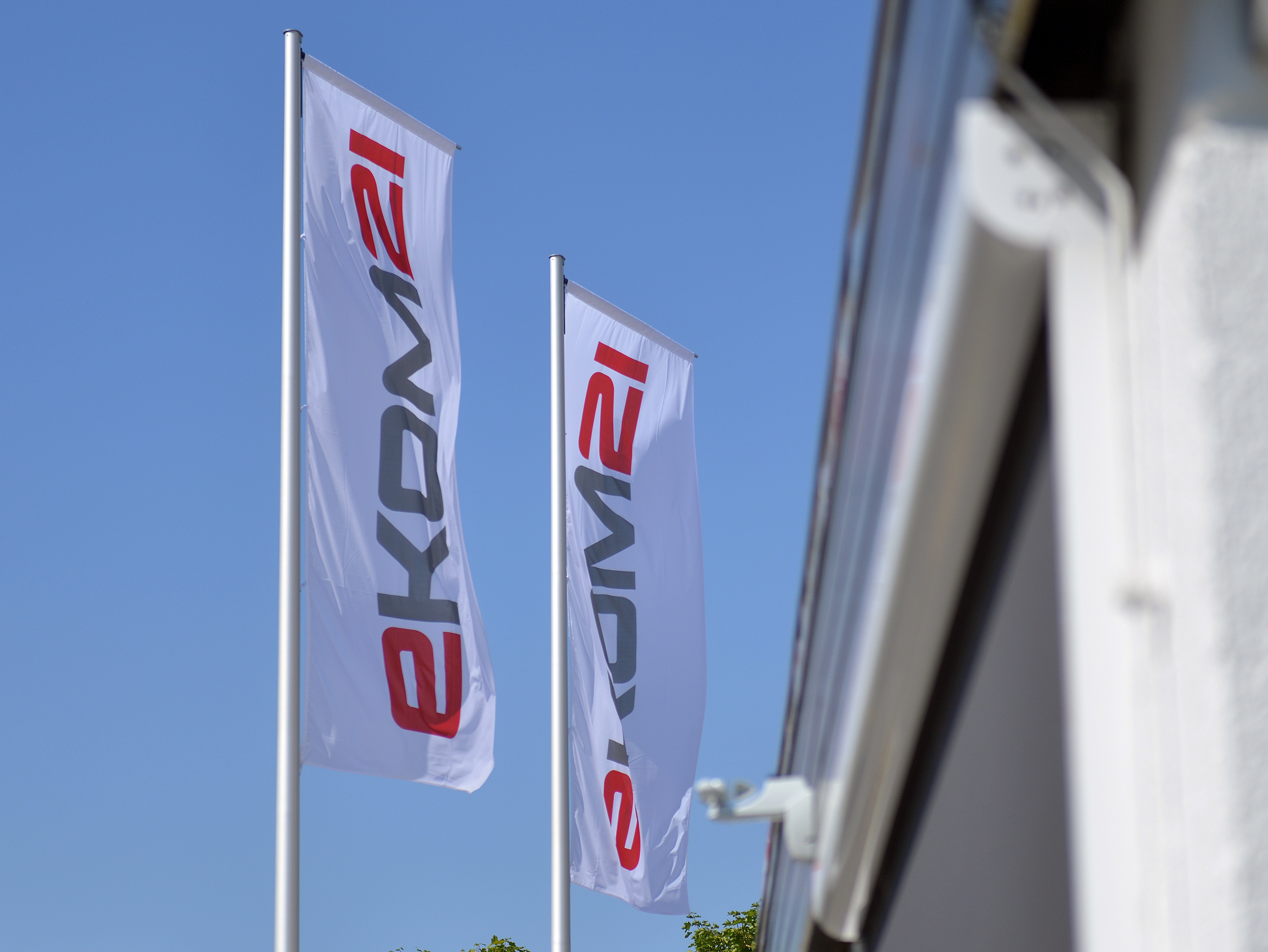 Zwei Fahnenmäste mit Fahnen; auf den Fahnen das Logo der ekom21